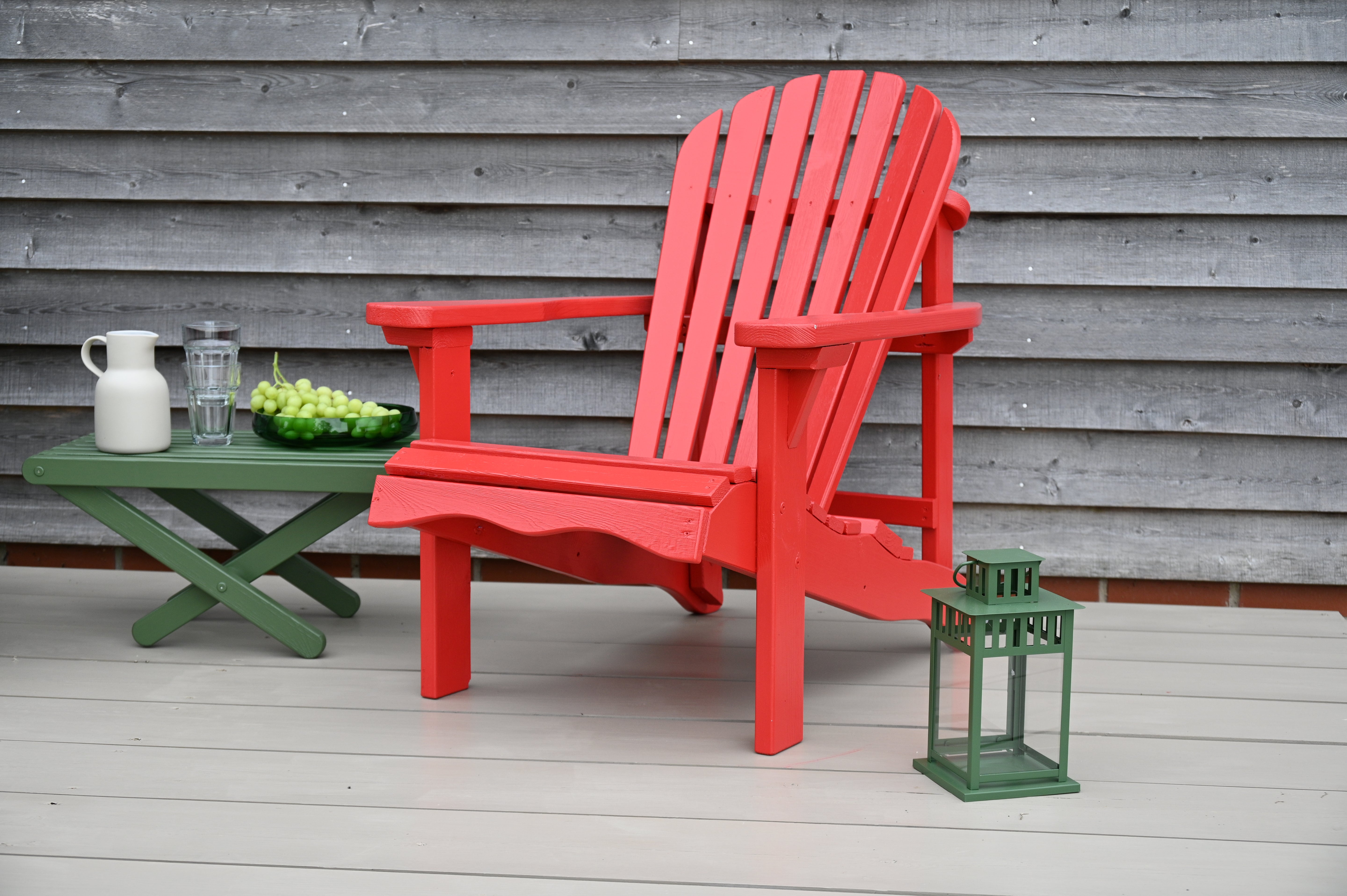 Nude Taupe Decking Stain, Red Royal Exterior Adirondack chair on a wooden deck with a green table and lantern