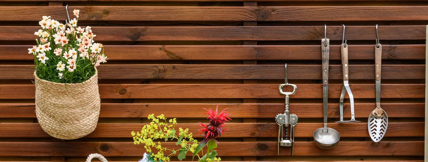 brown painted garden fence with flowers and tools hanging from it 